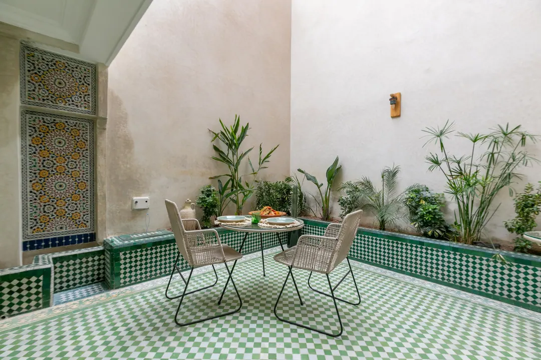 Planted patio with green-and-white zellige floor and woven chairs around a glass table