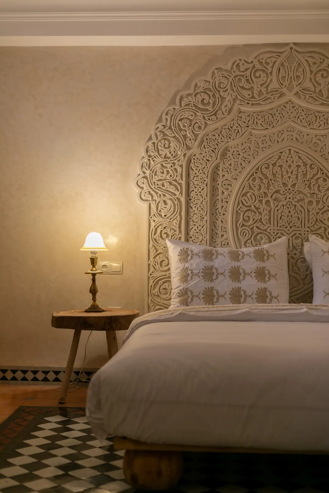 Ivory room: carved plaster headboard, bedside lamps and a black-and-white zellige floor