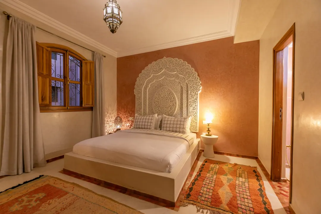 Terracotta room: carved white headboard on a rose-clay wall, cedar shutters and Berber rugs