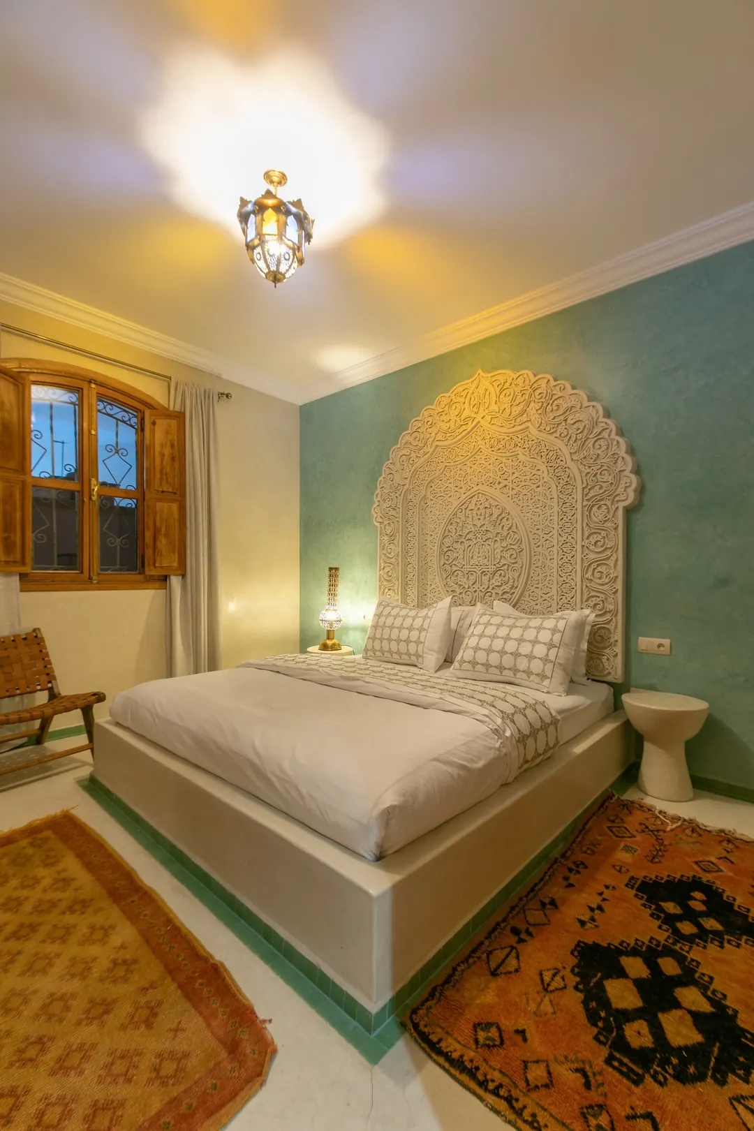 Jade room: king bed beneath a carved plaster headboard, pale jade tadelakt walls and Berber rug