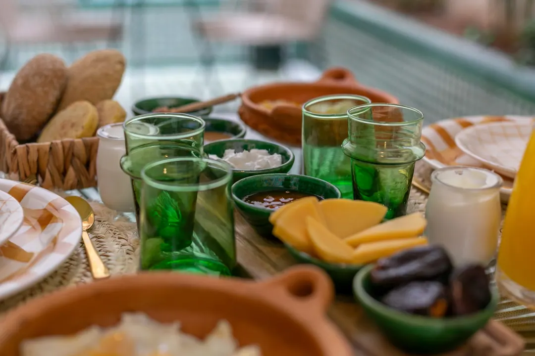 Detail of breakfast: green Beldi glasses, dates, cheese and fried eggs in a terracotta dish
