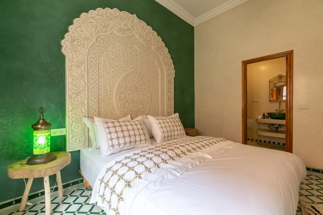 Emerald room: carved headboard on an emerald tadelakt wall, green lantern and zellige floor