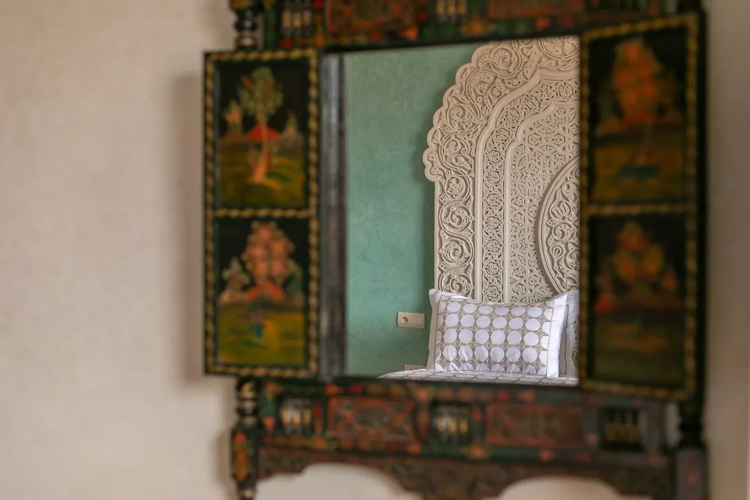 Jade room: king bed beneath a carved plaster headboard, pale jade tadelakt walls and Berber rug