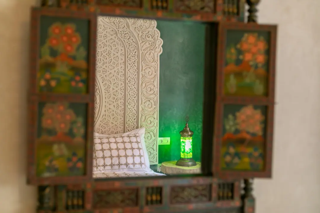 Emerald room: carved headboard on an emerald tadelakt wall, green lantern and zellige floor
