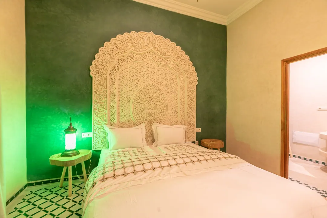 Emerald room: carved headboard on an emerald tadelakt wall, green lantern and zellige floor