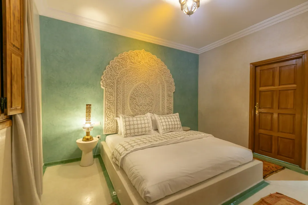 Jade room: king bed beneath a carved plaster headboard, pale jade tadelakt walls and Berber rug