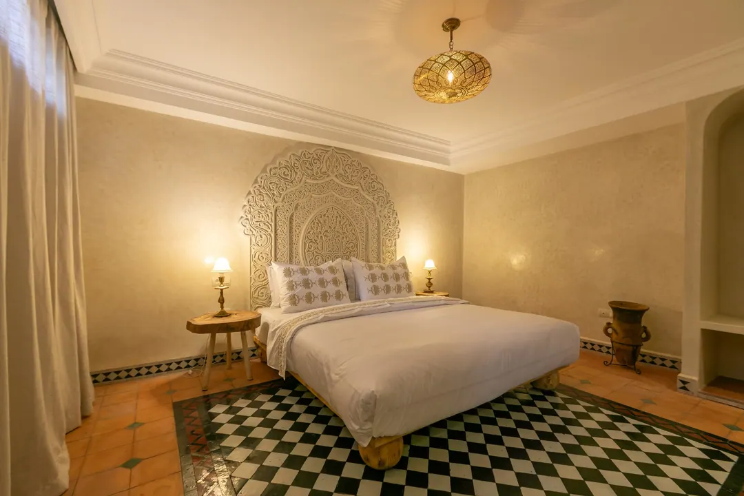 Ivory room: carved plaster headboard, bedside lamps and a black-and-white zellige floor