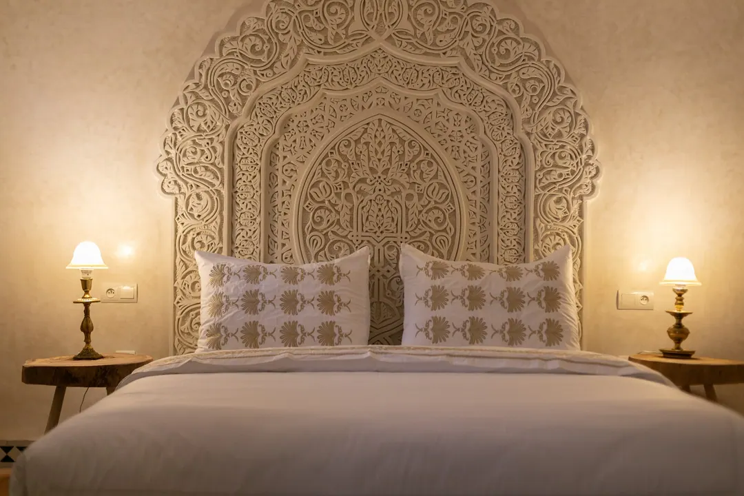 Ivory room: carved plaster headboard, bedside lamps and a black-and-white zellige floor