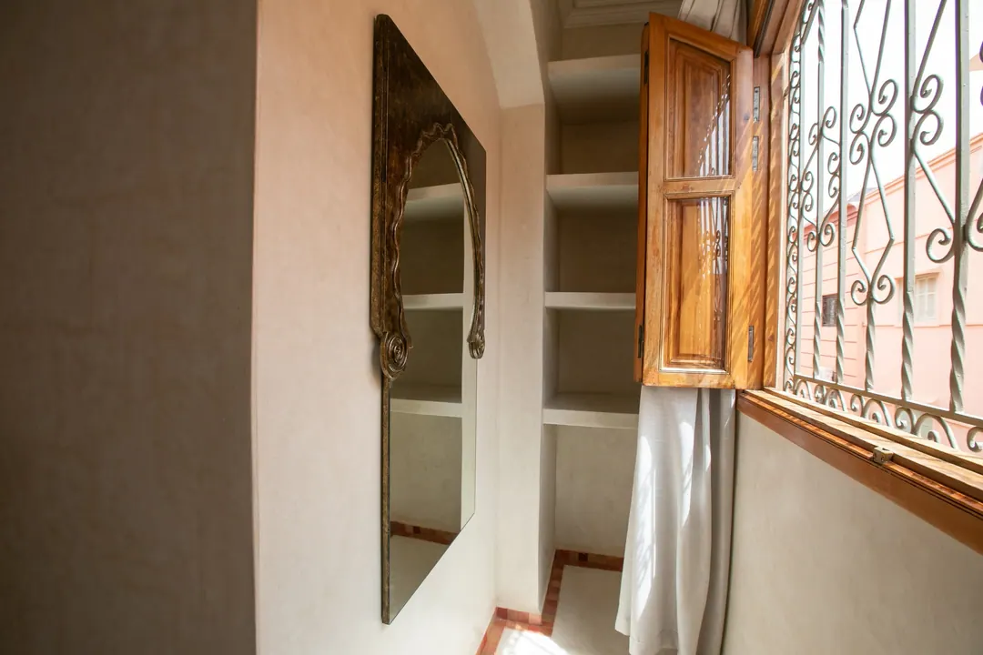 Terracotta room: carved white headboard on a rose-clay wall, cedar shutters and Berber rugs