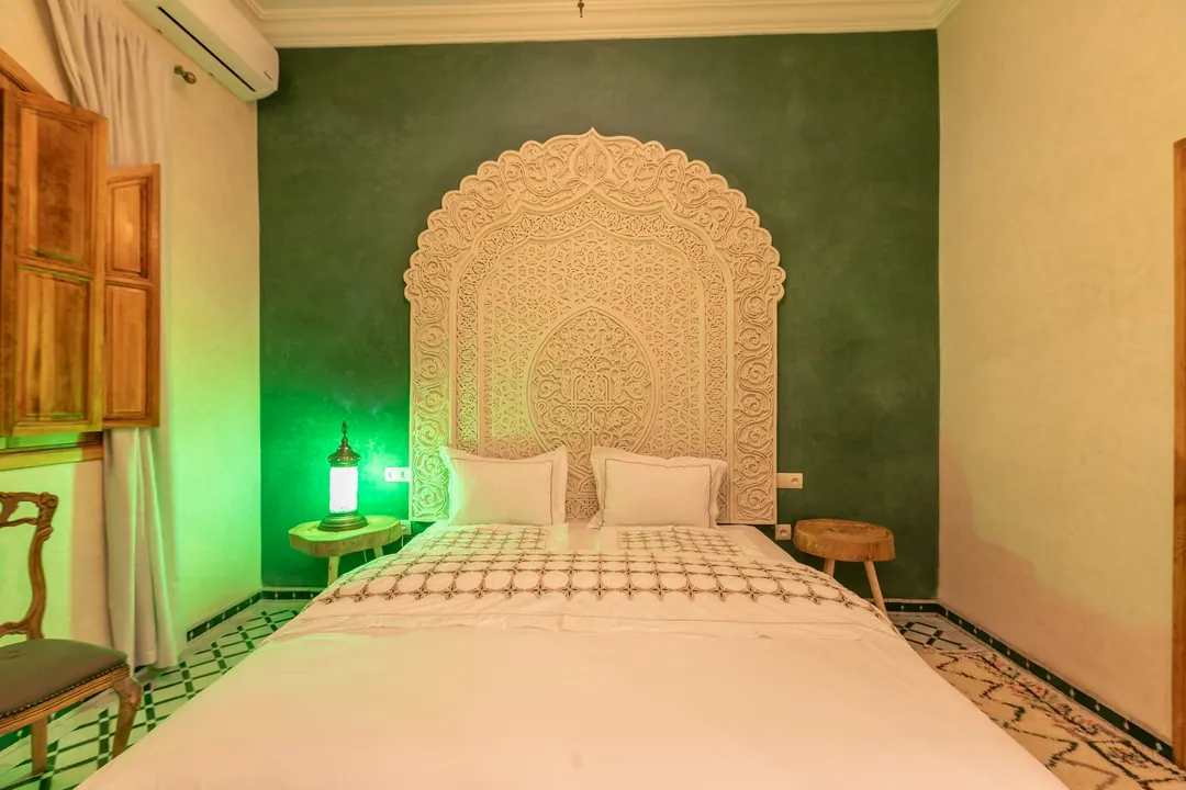 Emerald room: carved headboard on an emerald tadelakt wall, green lantern and zellige floor