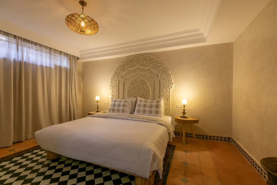 Ivory room: carved plaster headboard, bedside lamps and a black-and-white zellige floor