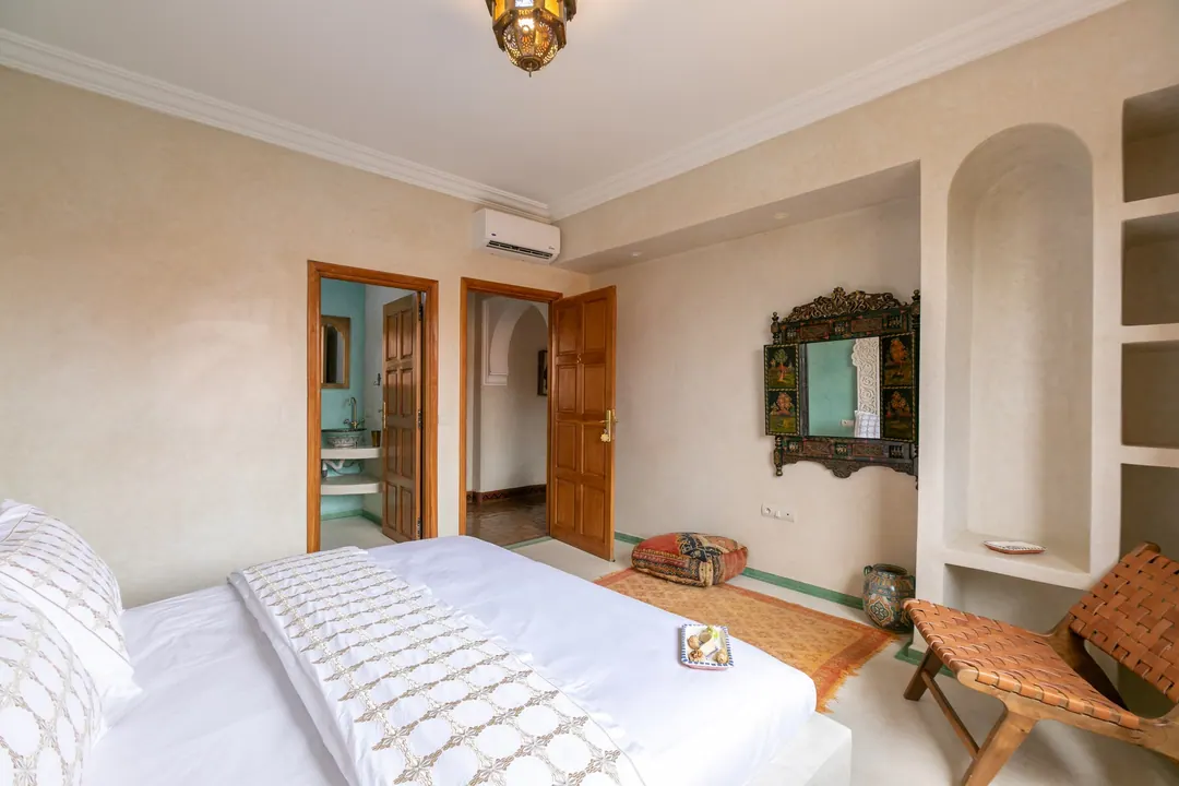 Jade room: king bed beneath a carved plaster headboard, pale jade tadelakt walls and Berber rug