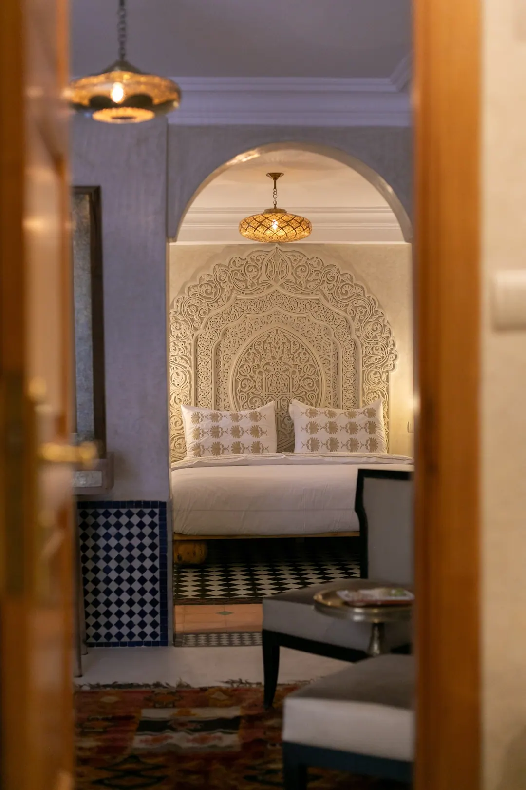 Ivory room: carved plaster headboard, bedside lamps and a black-and-white zellige floor