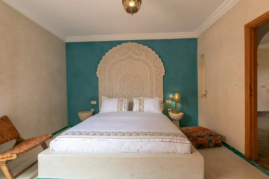 Turquoise room: carved plaster headboard against a deep turquoise wall, leather lounge chair