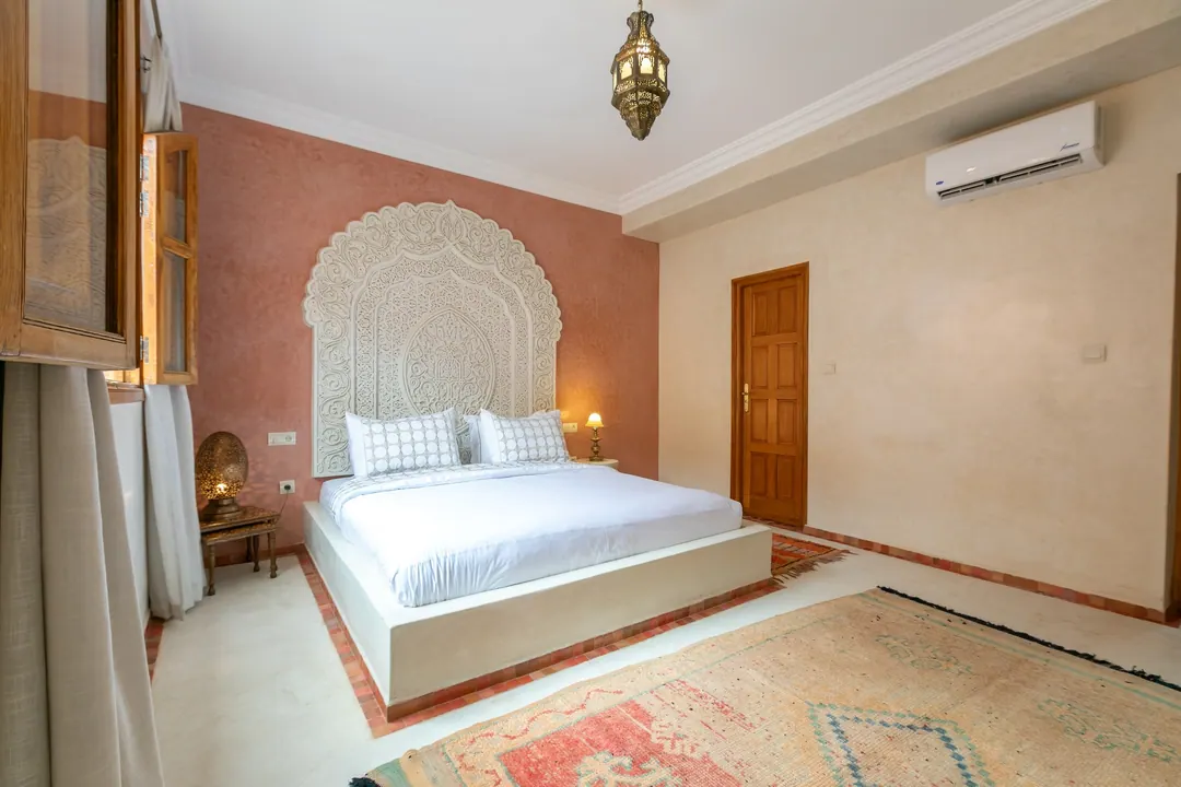 Terracotta room: carved white headboard on a rose-clay wall, cedar shutters and Berber rugs