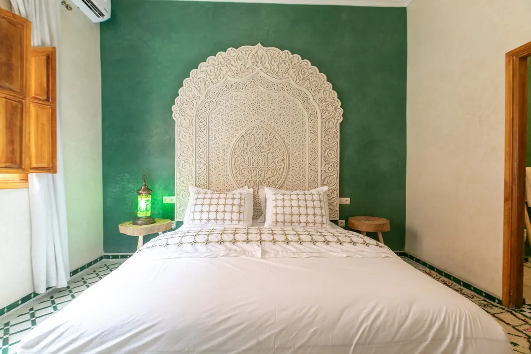 Emerald room: carved headboard on an emerald tadelakt wall, green lantern and zellige floor