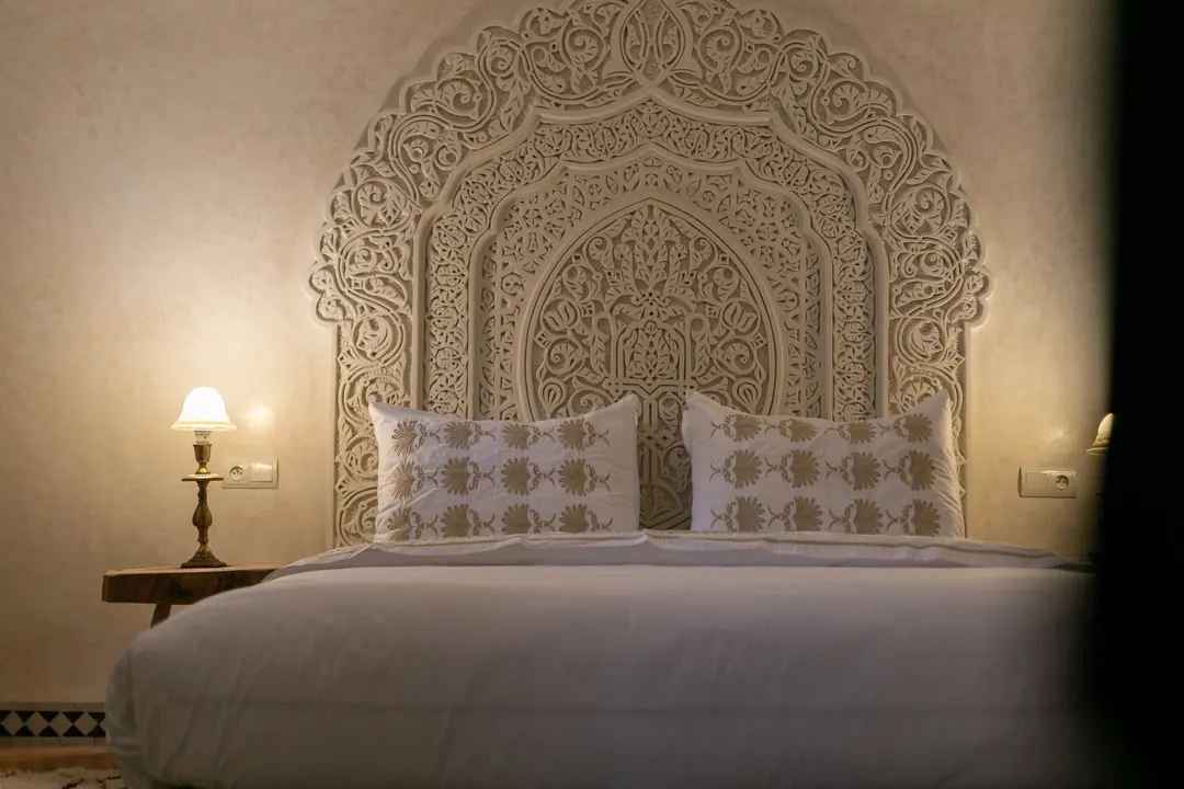Ivory room: carved plaster headboard, bedside lamps and a black-and-white zellige floor
