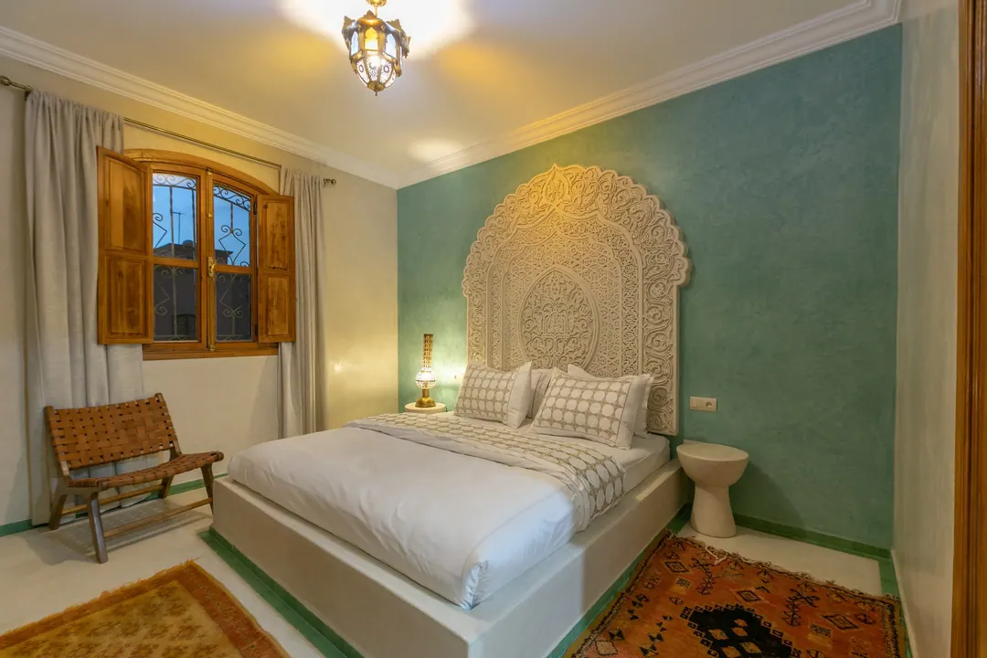Jade room: king bed beneath a carved plaster headboard, pale jade tadelakt walls and Berber rug