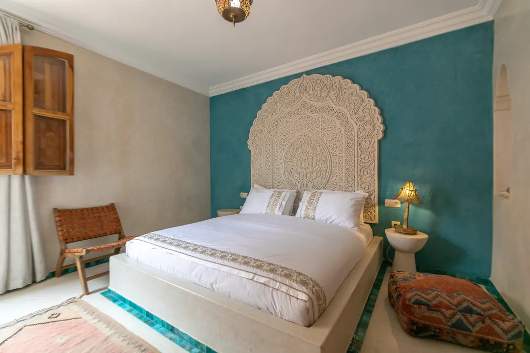 Turquoise room: carved plaster headboard against a deep turquoise wall, leather lounge chair