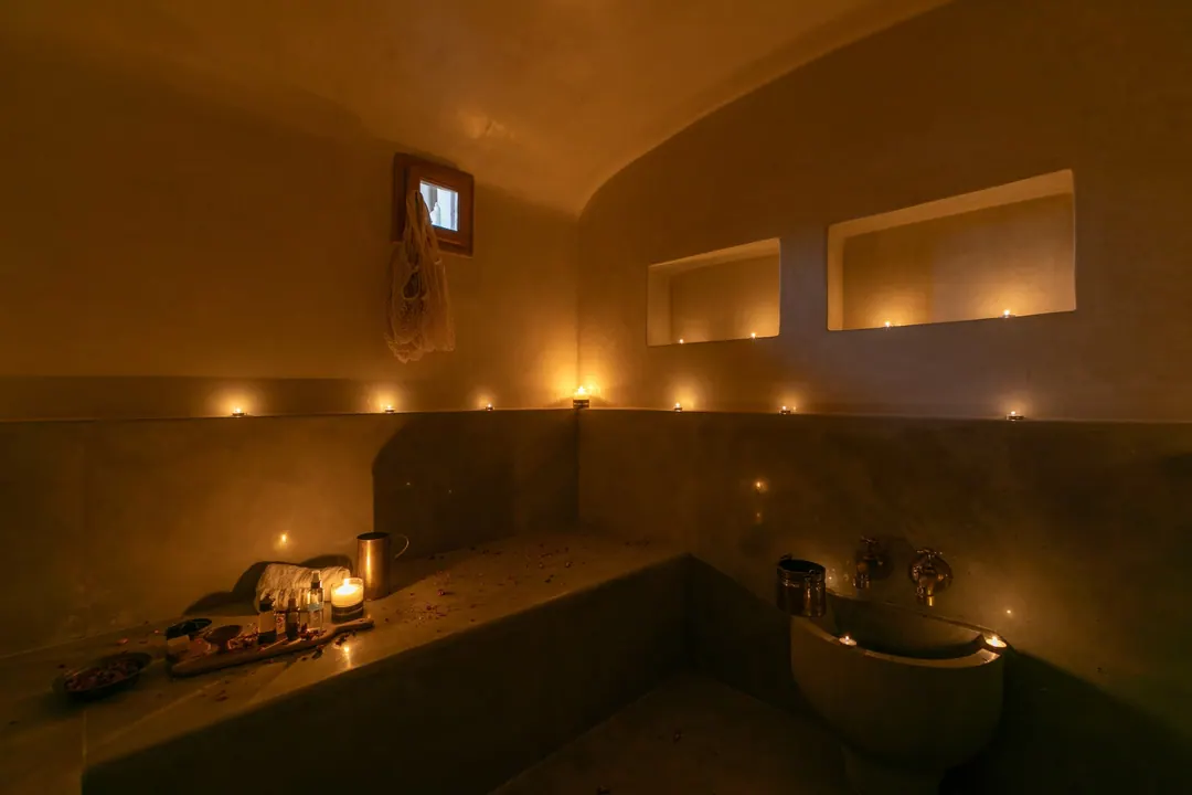 Candle-lit tadelakt hammam with a heated stone bench and copper basin