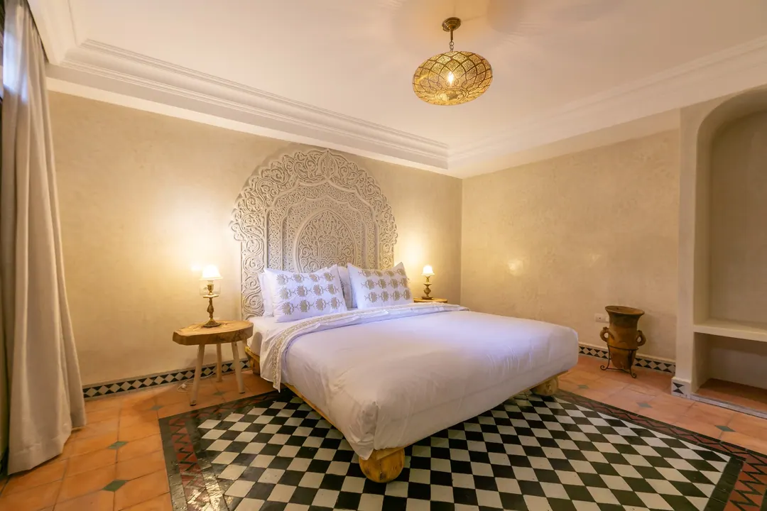Ivory room: carved plaster headboard, bedside lamps and a black-and-white zellige floor