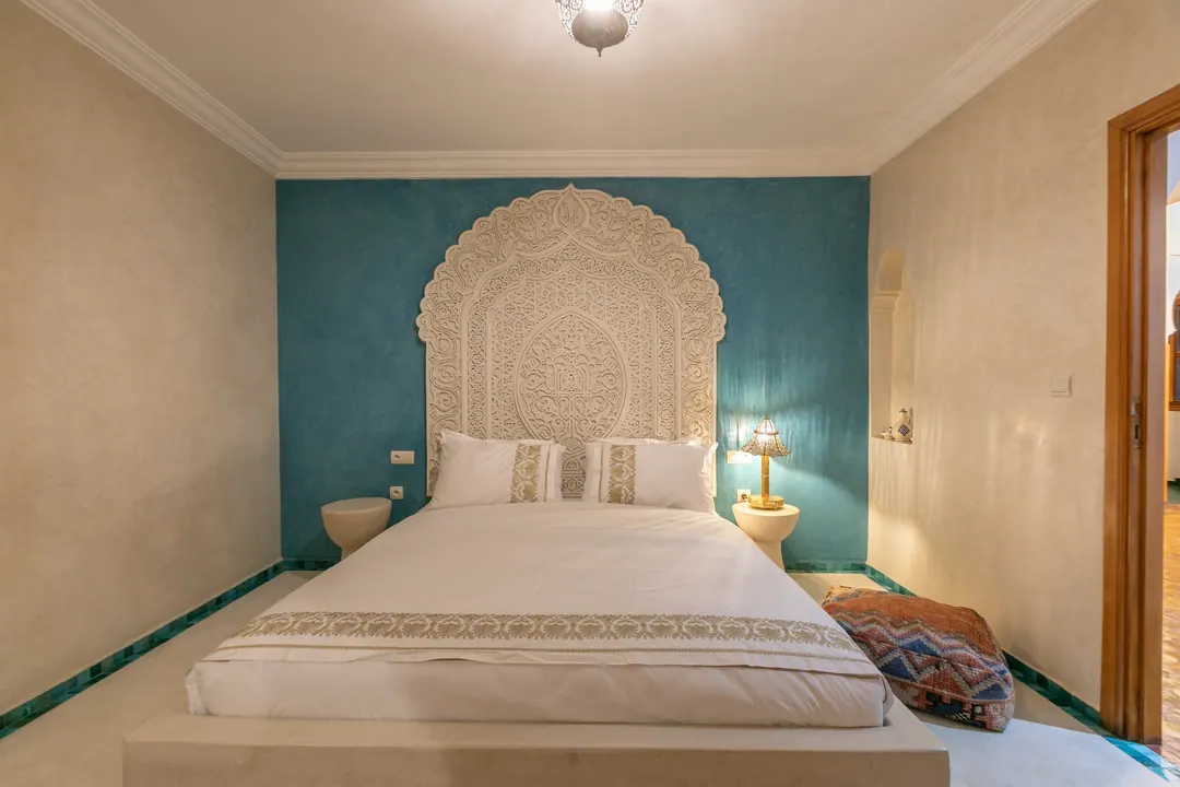 Turquoise room: carved plaster headboard against a deep turquoise wall, leather lounge chair