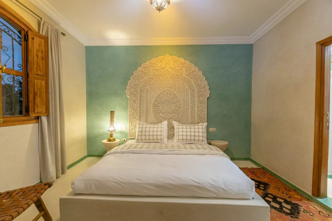 Jade room: king bed beneath a carved plaster headboard, pale jade tadelakt walls and Berber rug