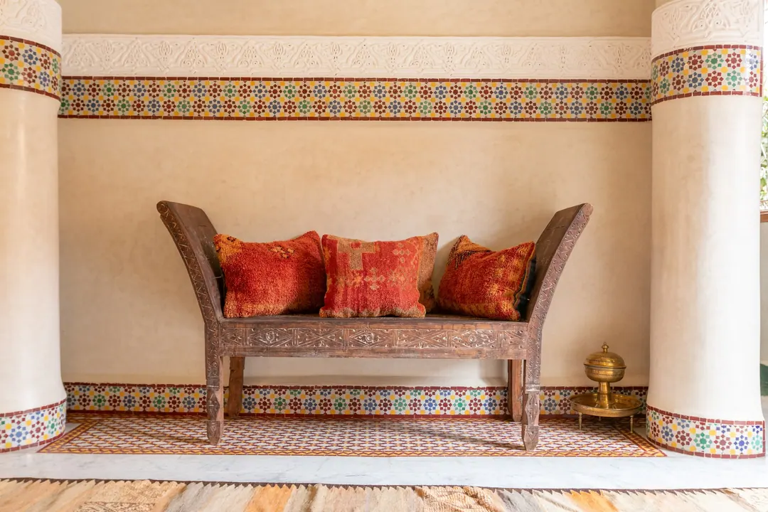Antique carved bench with red cushions beneath a band of zellige tiles