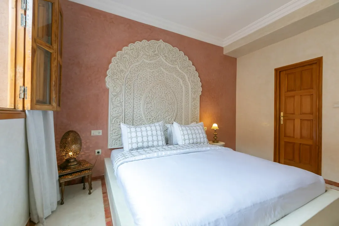 Terracotta room: carved white headboard on a rose-clay wall, cedar shutters and Berber rugs