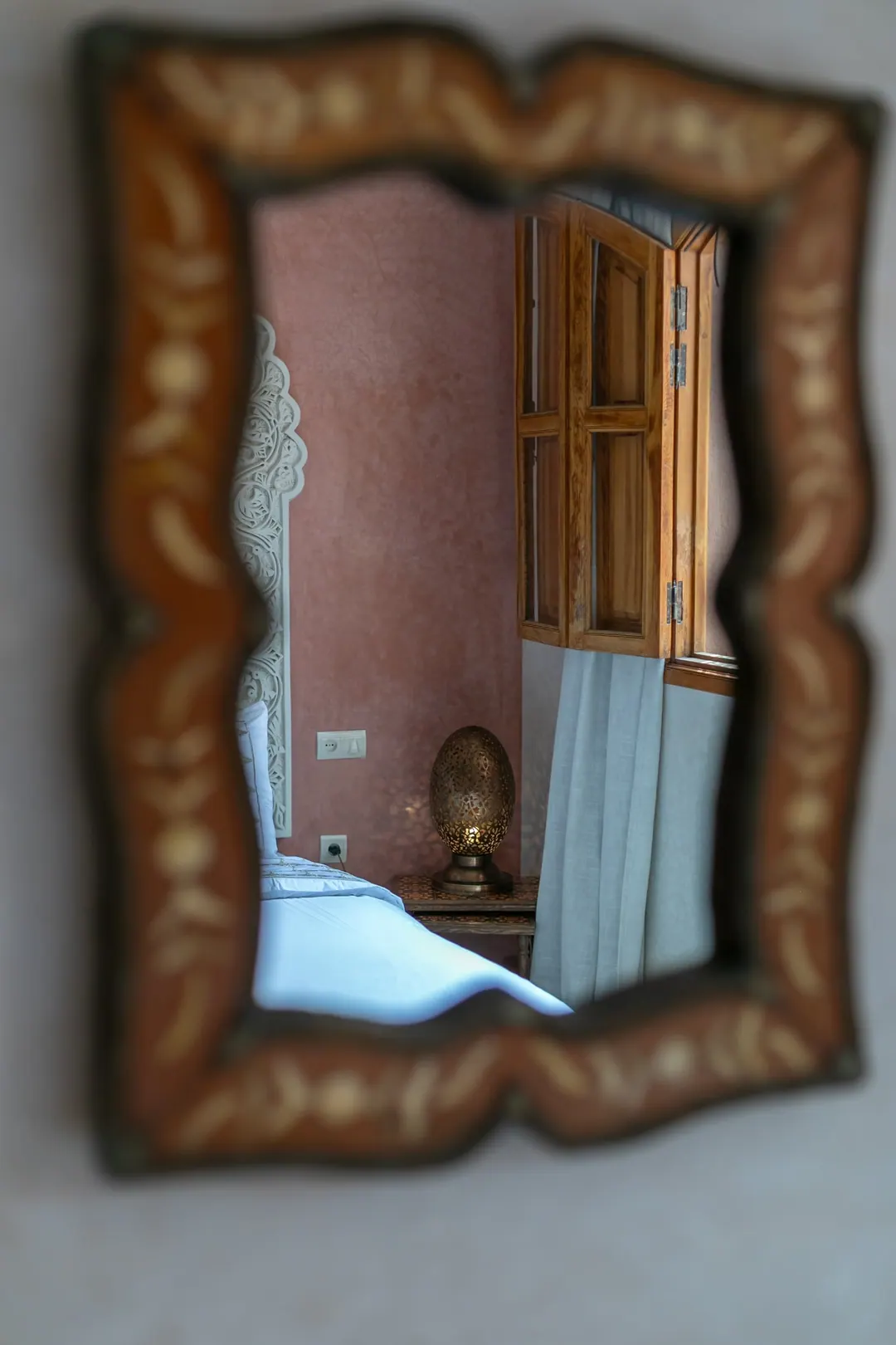 Terracotta room: carved white headboard on a rose-clay wall, cedar shutters and Berber rugs