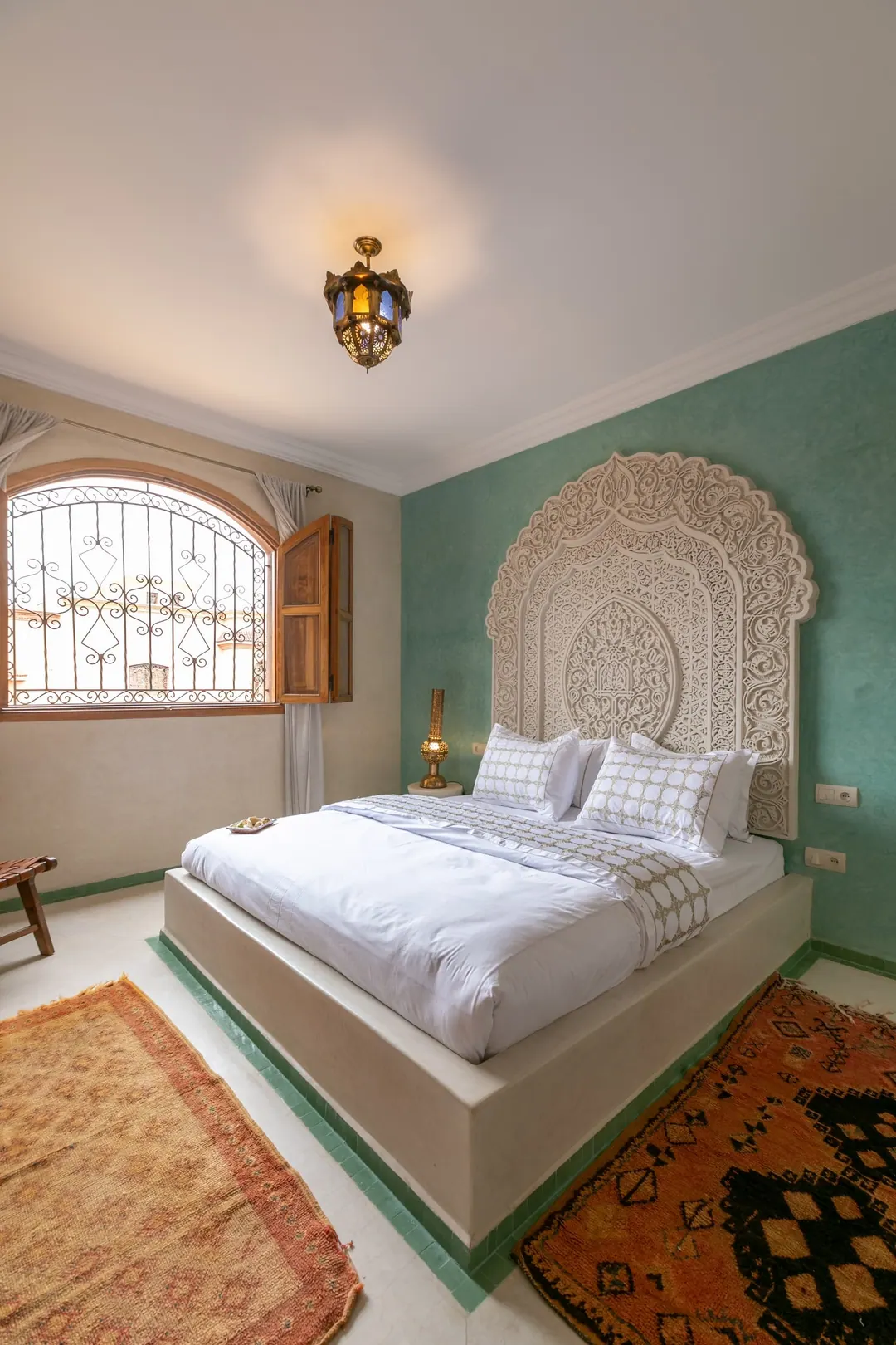 Jade room: king bed beneath a carved plaster headboard, pale jade tadelakt walls and Berber rug