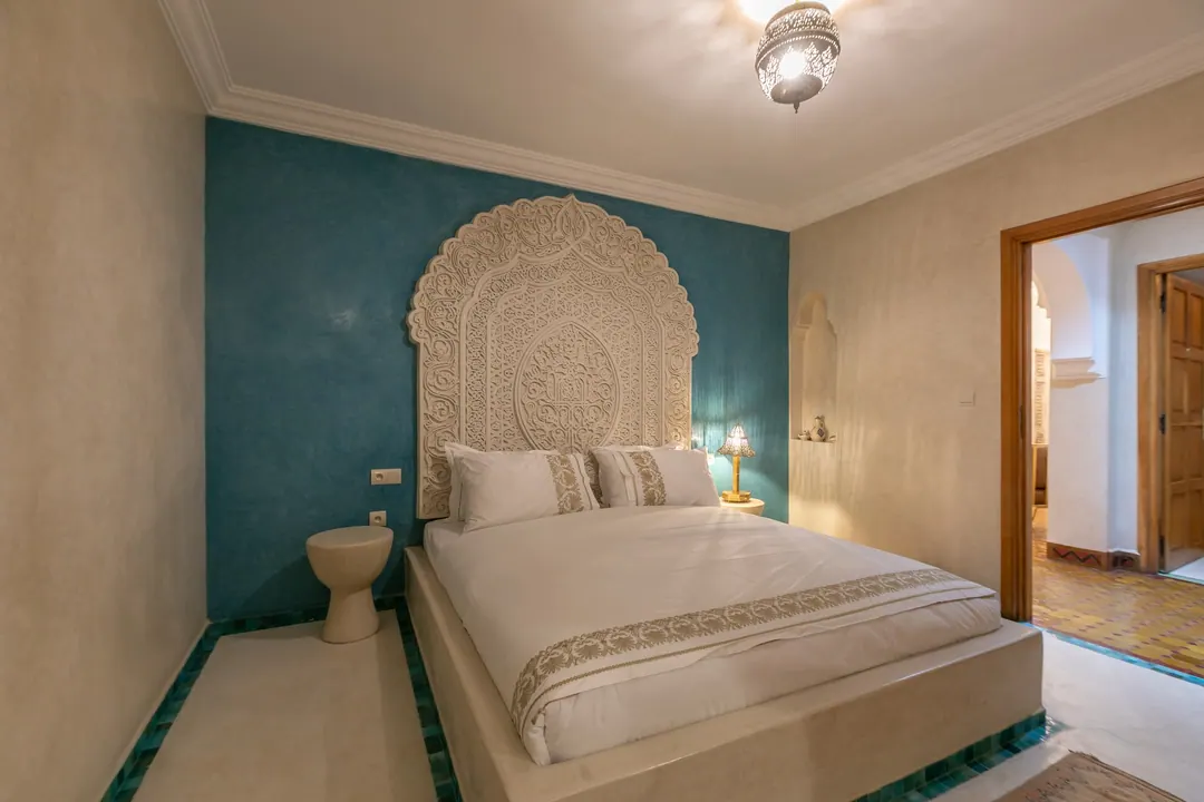 Turquoise room: carved plaster headboard against a deep turquoise wall, leather lounge chair