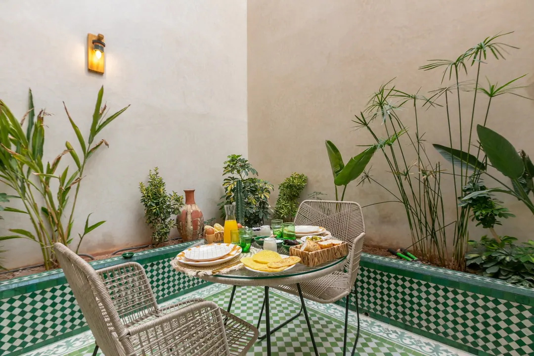 Planted patio with green-and-white zellige floor and woven chairs around a glass table