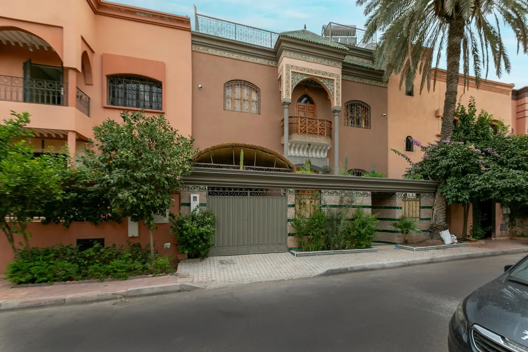 Terracotta façade of the riad with a carved balcony and palm trees
