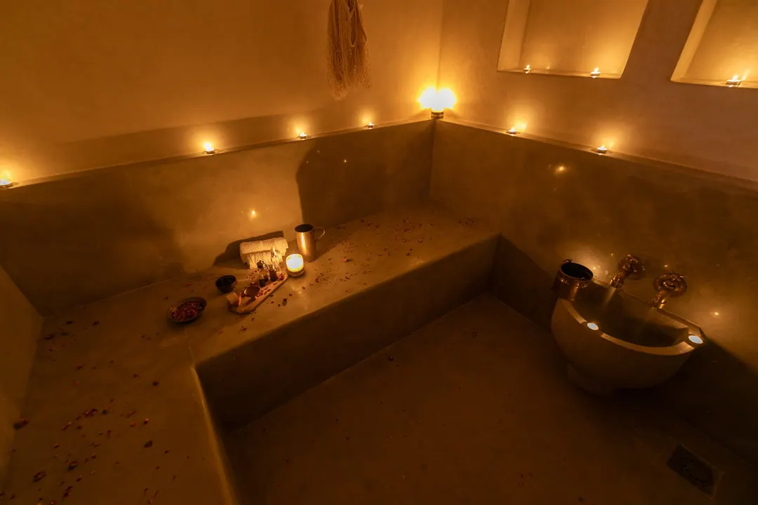 Candle-lit tadelakt hammam with a heated stone bench and copper basin