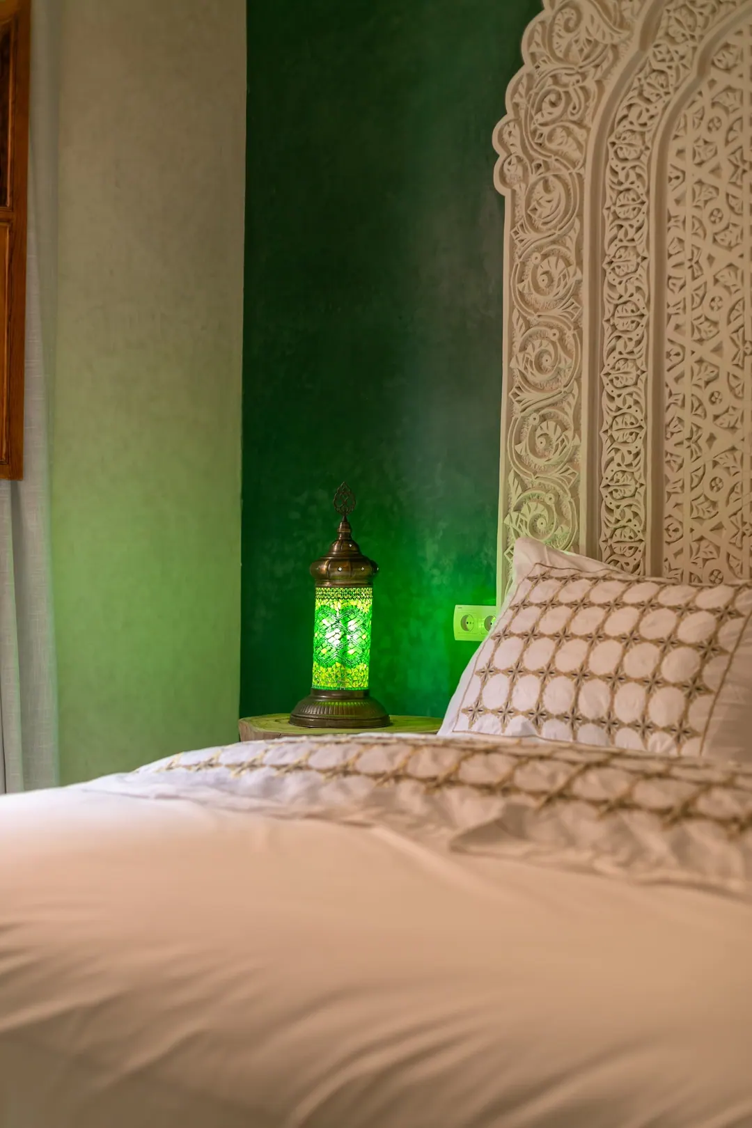 Emerald room: carved headboard on an emerald tadelakt wall, green lantern and zellige floor