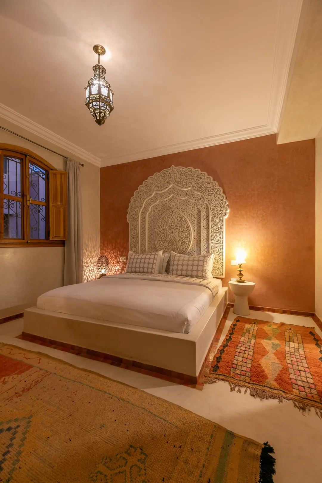 Terracotta room: carved white headboard on a rose-clay wall, cedar shutters and Berber rugs