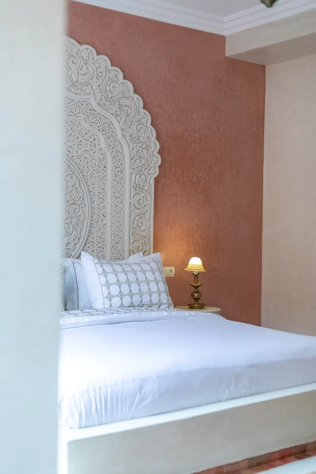 Terracotta room: carved white headboard on a rose-clay wall, cedar shutters and Berber rugs