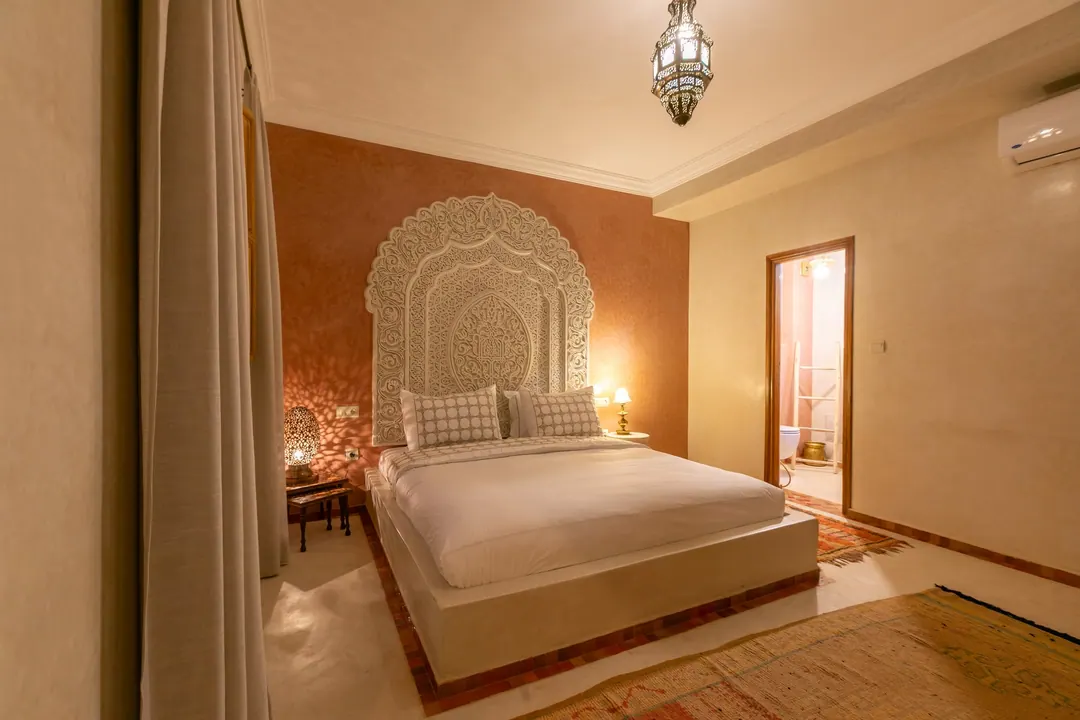 Terracotta room: carved white headboard on a rose-clay wall, cedar shutters and Berber rugs