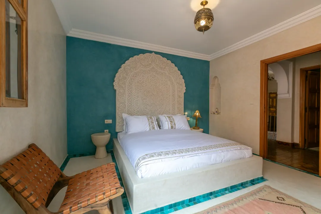 Turquoise room: carved plaster headboard against a deep turquoise wall, leather lounge chair