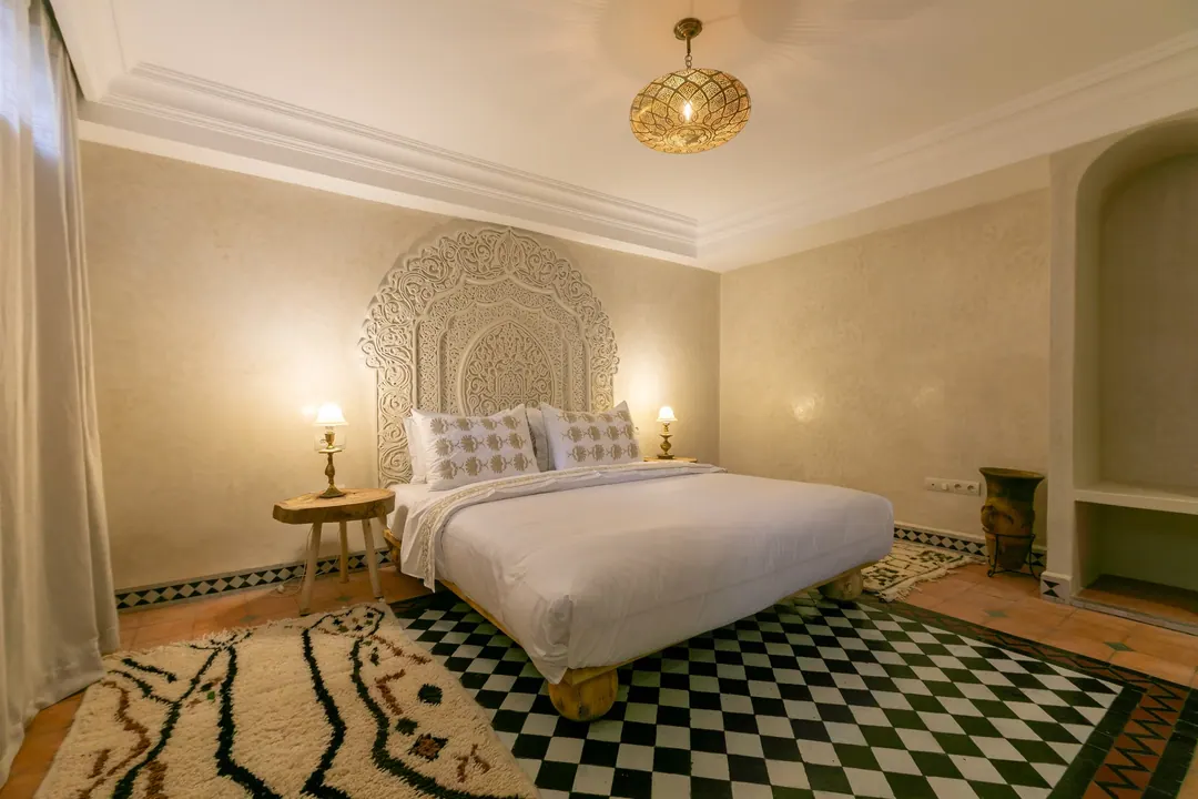 Ivory room: carved plaster headboard, bedside lamps and a black-and-white zellige floor