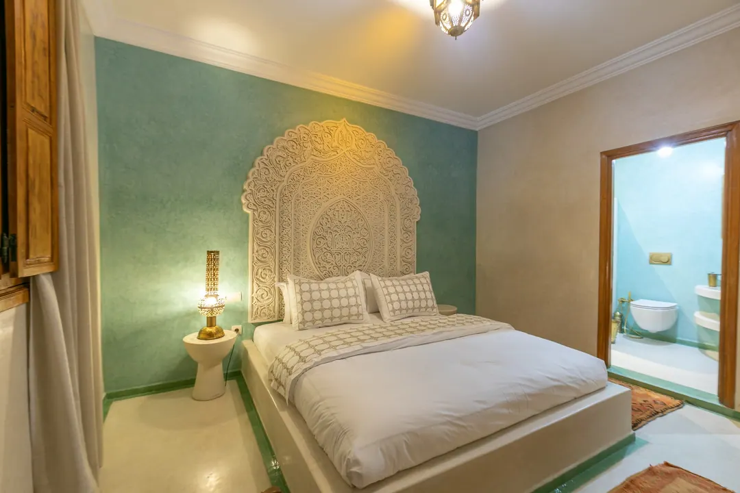 Jade room: king bed beneath a carved plaster headboard, pale jade tadelakt walls and Berber rug