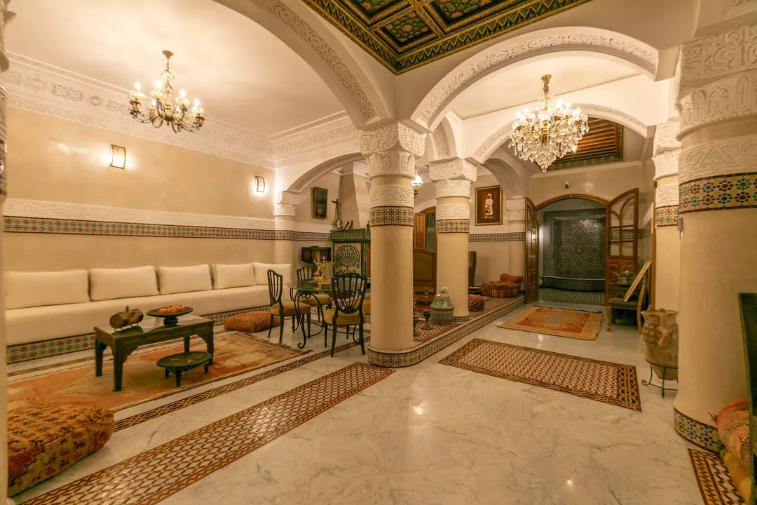The salon at night under glowing chandeliers and a painted cedar ceiling