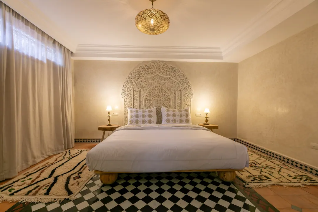 Ivory room: carved plaster headboard, bedside lamps and a black-and-white zellige floor