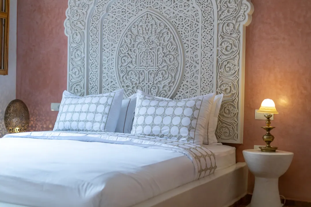 Terracotta room: carved white headboard on a rose-clay wall, cedar shutters and Berber rugs