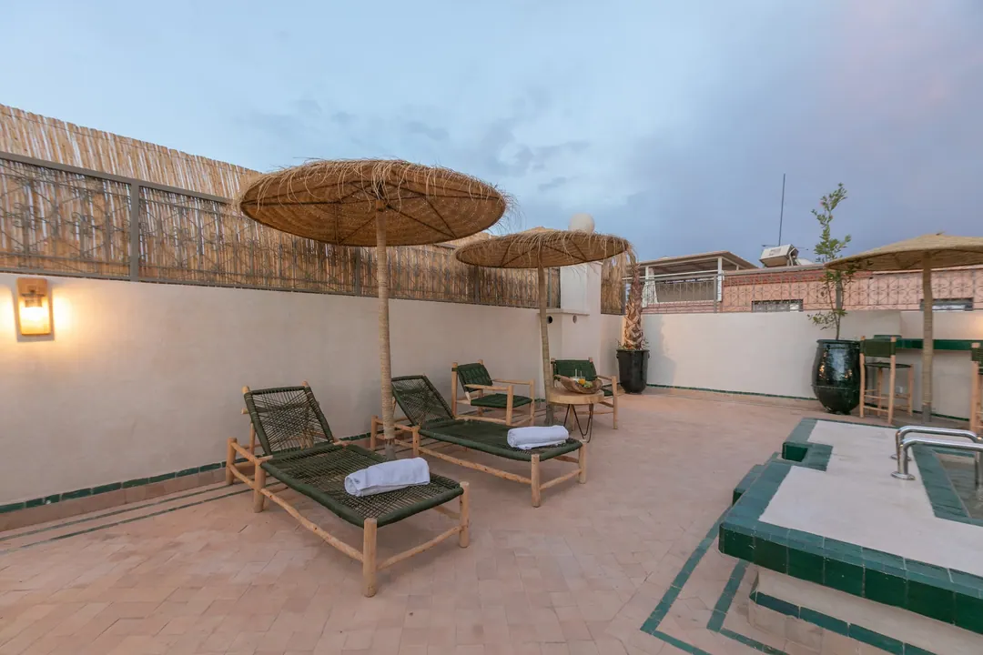 Cedar and green-cord sun loungers under reed parasols on the rooftop