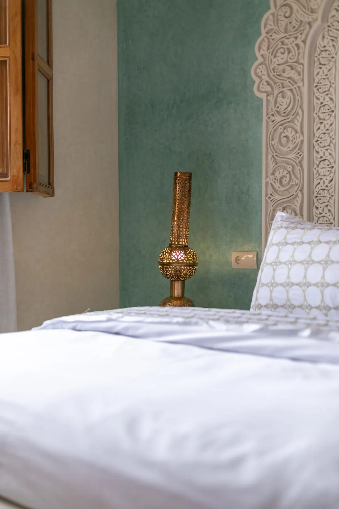 Jade room: king bed beneath a carved plaster headboard, pale jade tadelakt walls and Berber rug