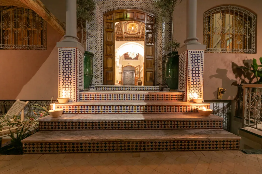 Candle-lit tiled steps leading to the carved wooden door of the riad at night