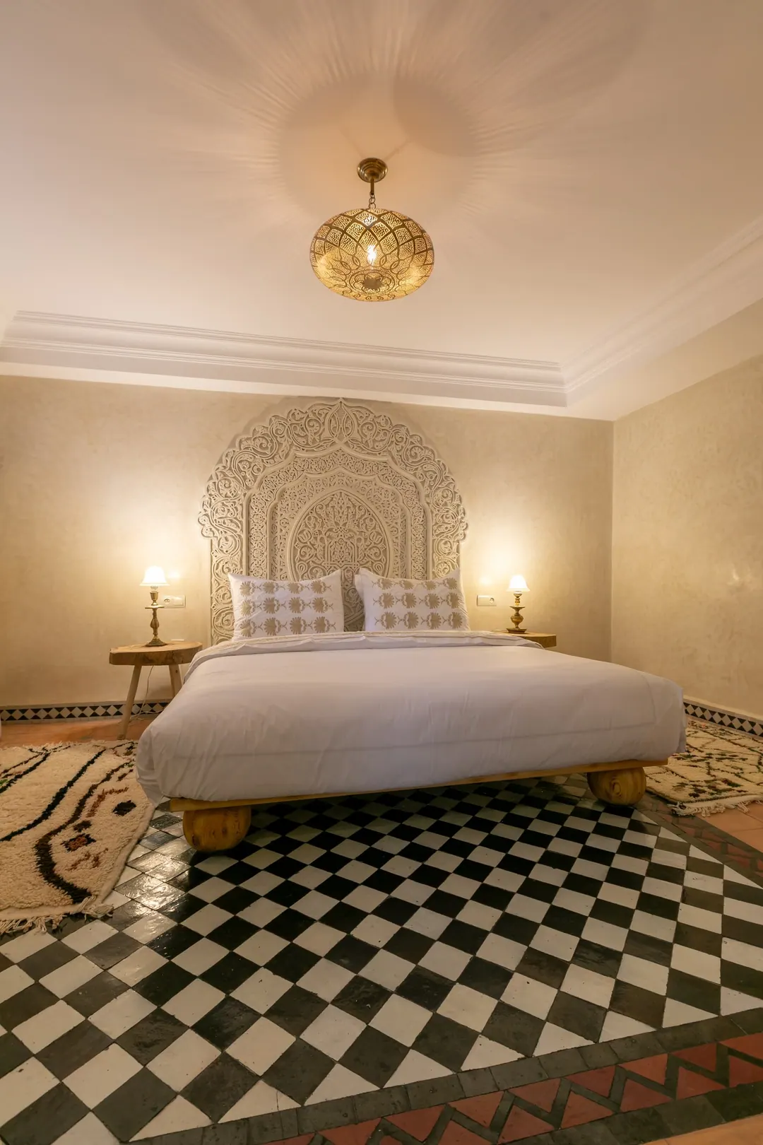 Ivory room: carved plaster headboard, bedside lamps and a black-and-white zellige floor