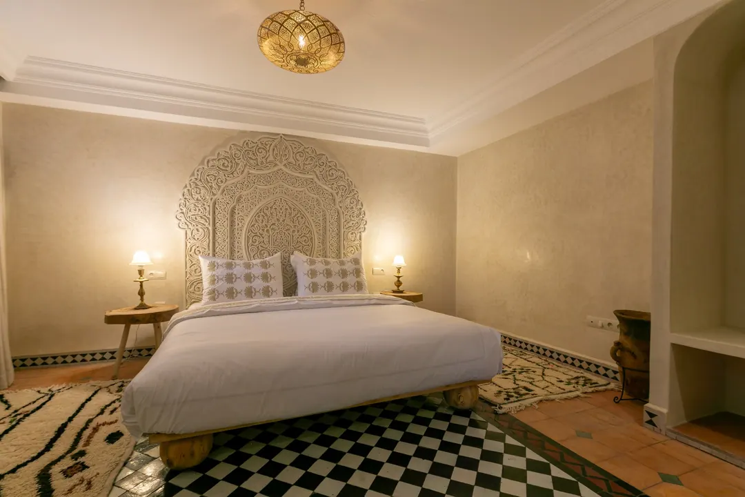 Ivory room: carved plaster headboard, bedside lamps and a black-and-white zellige floor